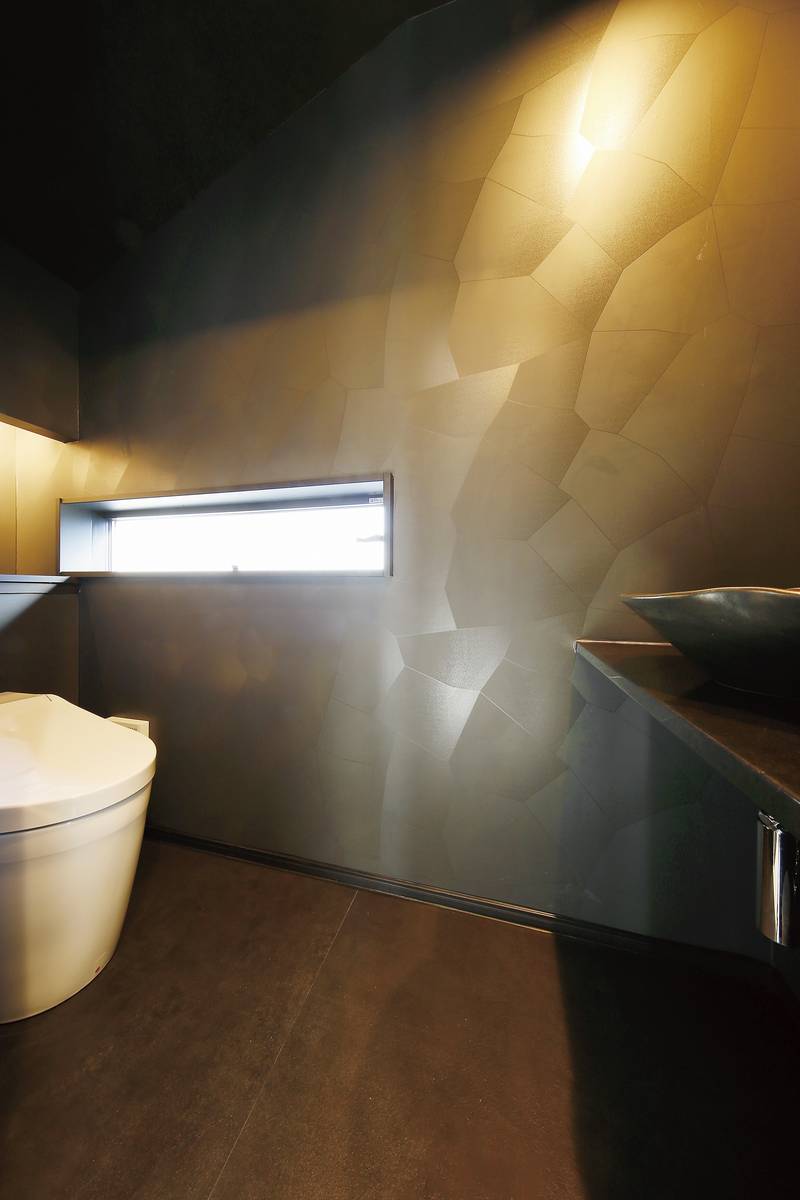 凹凸のある壁面が光を反射して独特の雰囲気を演出するトイレは、洗面器や配管にもこだわっています。
